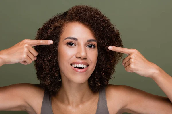 Portrait of african american woman pointing with fingers at eyes isolated on green — Stock Photo