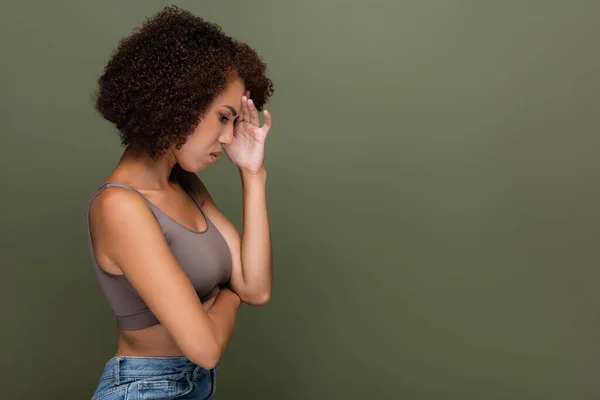 Side view of upset african american woman in top touching forehead isolated on green — Stock Photo