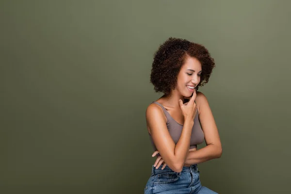 Positiva donna afro-americana in alto toccando mento isolato sul verde — Foto stock