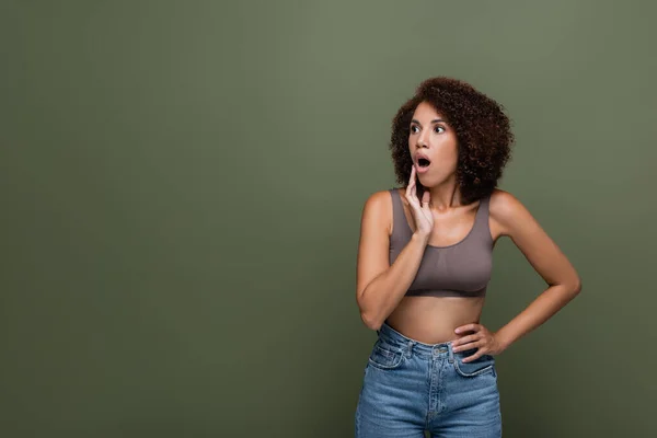 Shocked african american woman in top holding hand on hip and looking away isolated on green — Stock Photo