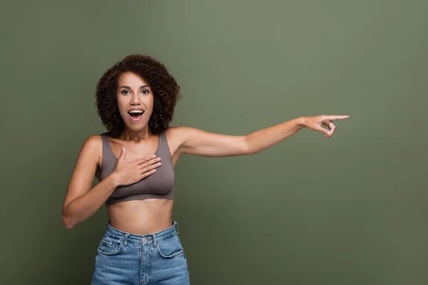 Positive afrikanisch-amerikanische Frau in Top-Berührung der Brust und Zeigen mit dem Finger isoliert auf grün — Stockfoto
