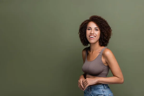 Pretty african american woman in top and jeans looking at camera isolated on green — Stock Photo