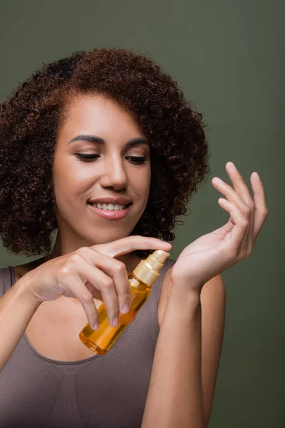 Positiva donna afro-americana che applica olio cosmetico a portata di mano isolato sul verde — Foto stock