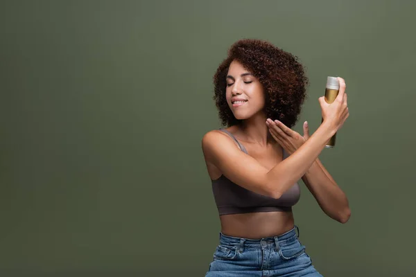 Smiling african american woman applying hairspray isolated on green — Stock Photo