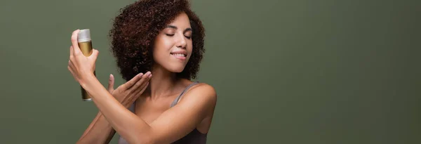 Hübsche Afroamerikanerin trägt Haarspray isoliert auf grünem Banner auf — Stockfoto