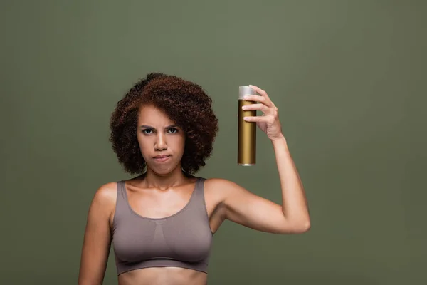 Sad african american model in top holding hairspray isolated on green — Stock Photo