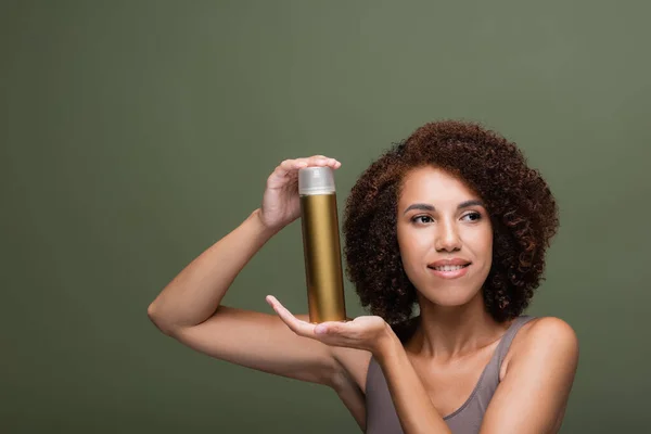 Улыбающаяся африканская американка держит лак для волос и смотрит в сторону изолированной на зеленый — стоковое фото