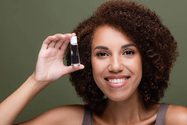 Retrato de mujer afroamericana sosteniendo aceite cosmético aislado en verde - foto de stock