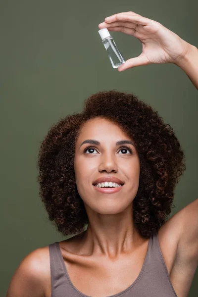 Красивая и кудрявая африканская американка, смотрящая на косметическое масло, изолированное на зеленом — стоковое фото