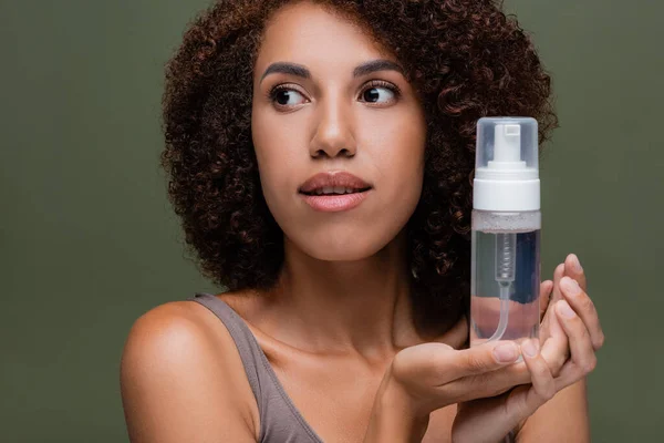 Portrait of curly african american woman holding cleansing foam isolated on green — Stock Photo