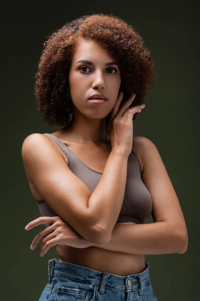 Porträt einer lockigen afrikanisch-amerikanischen Frau in Top-Pose und Blick in die Kamera isoliert auf dunkelgrün — Stockfoto