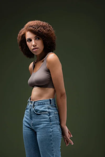 Joven mujer afroamericana en la parte superior y jeans posando aislado en verde oscuro - foto de stock