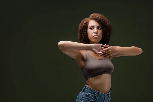 Young and curly african american model in top touching hands isolated on dark green — Stock Photo