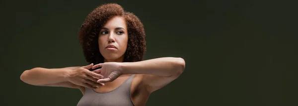 Femme afro-américaine bouclée dans les mains touchantes supérieures isolées sur vert foncé, bannière — Photo de stock