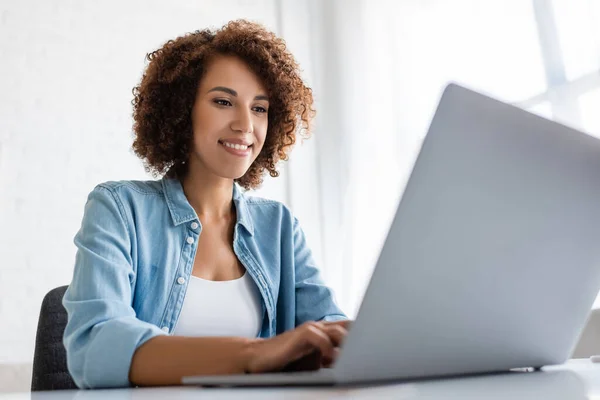 Freelancer afro-americano positivo usando laptop borrado em casa — Fotografia de Stock