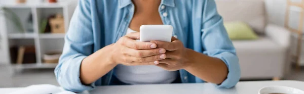 Cropped view of african american woman in casual clothes using smartphone near cup of tea at home, banner — Stock Photo