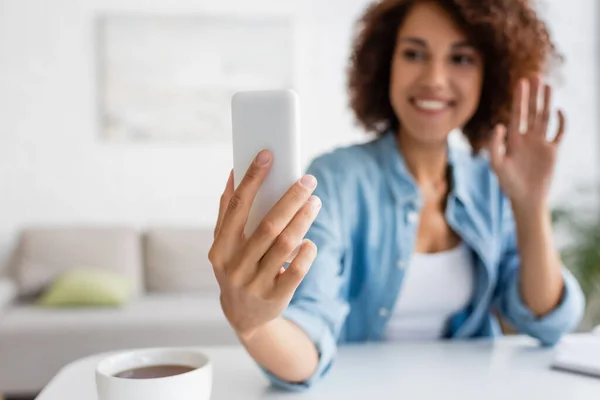 Mulher americana africana desfocada ter chamada de vídeo no smartphone perto da xícara de chá em casa — Fotografia de Stock