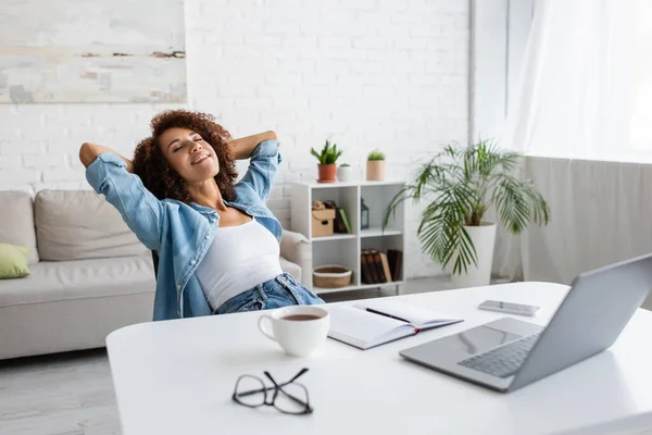 Mulher americana africana alegre com olhos fechados descansando perto do local de trabalho em casa — Fotografia de Stock