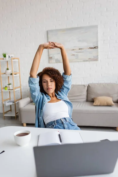 Tired african american woman with curly hair stretching near workplace at home — Stock Photo