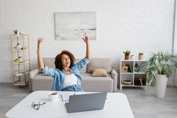 Pleased african american woman with closed eyes rejoicing near workplace at home — Stock Photo