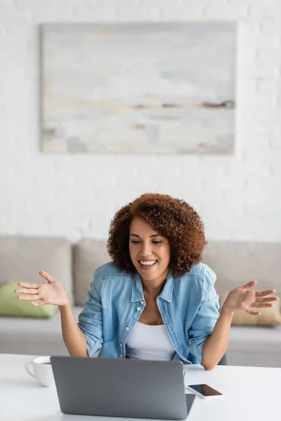 Cheerful and curly african american freelancer gesturing during video call on laptop — Stock Photo