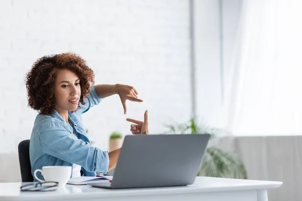 Encaracolado Africano americano mulher mostrando forma quadrada com as mãos durante chamada de vídeo no laptop — Fotografia de Stock