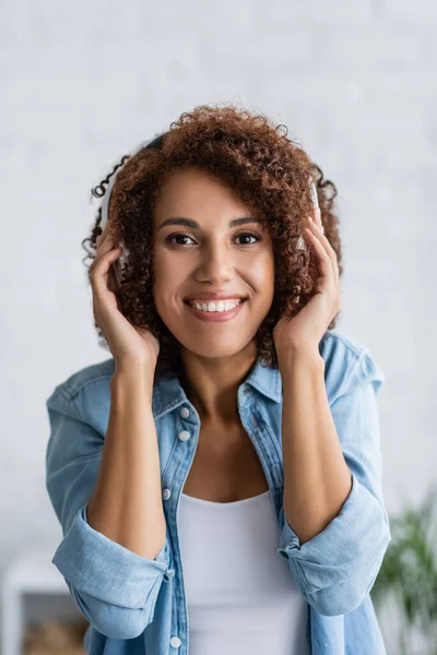 Alegre mujer afroamericana sonriendo mientras escucha música en auriculares inalámbricos - foto de stock