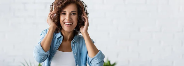 Mujer afroamericana positiva sonriendo mientras escucha música en auriculares inalámbricos, pancarta - foto de stock