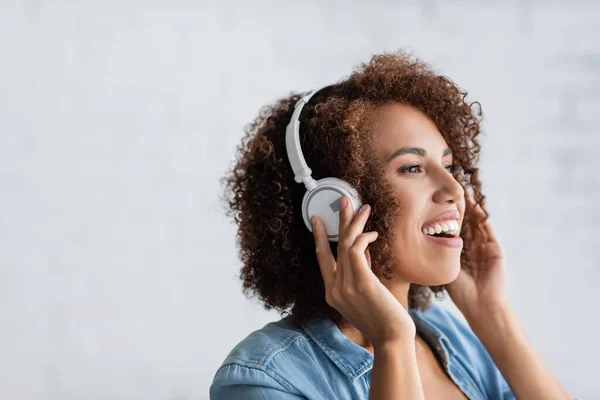 Excited african american woman smiling while listening music in wireless headphones — Stock Photo