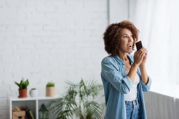 Excited african american woman holding smartphone with blank screen and looking away — Stock Photo