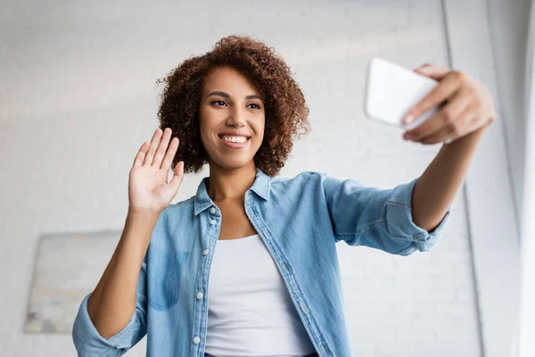 Felice donna africana americana con i capelli ricci agitando la mano durante la videochiamata su smartphone — Foto stock