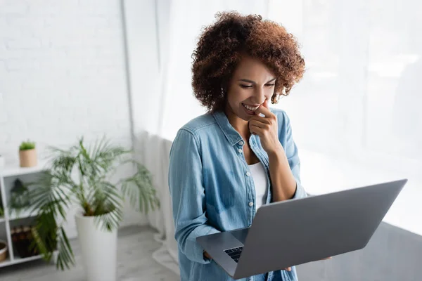 Positive afrikanisch-amerikanische Frau mit lockigem Haar hält Laptop während der Arbeit von zu Hause aus — Stockfoto