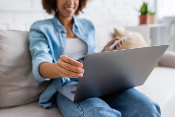 Vista recortada de la mujer afroamericana usando el ordenador portátil mientras está sentado en el sofá - foto de stock