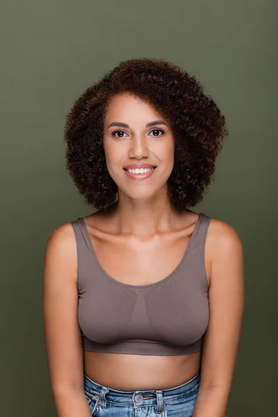 Happy and curly african american woman in crop top looking at camera isolated on green — Stock Photo