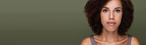 Portrait of curly african american woman looking at camera isolated on green, banner — Stock Photo