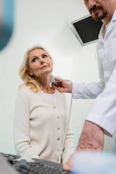 Visão de baixo ângulo da mulher madura perto do médico fazendo exame de ultra-som em primeiro plano turvo — Fotografia de Stock