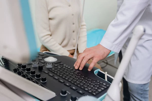 Vue recadrée du médecin en utilisant le panneau de commande de la machine à ultrasons près de la femme en clinique — Photo de stock