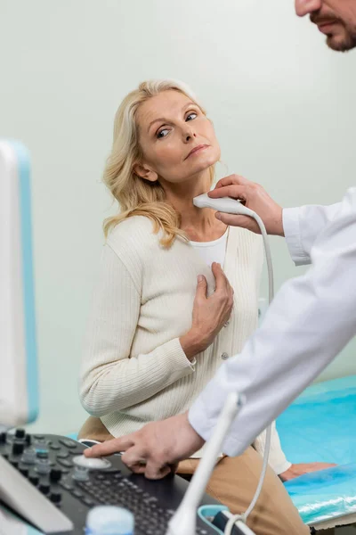 Mujer rubia mirando la máquina de ultrasonido cerca del médico haciendo diagnósticos de su laringe - foto de stock