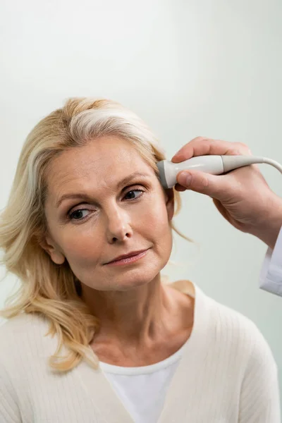 Bastante mujer de mediana edad cerca del médico haciendo ultrasonido examen neurológico de su cabeza - foto de stock