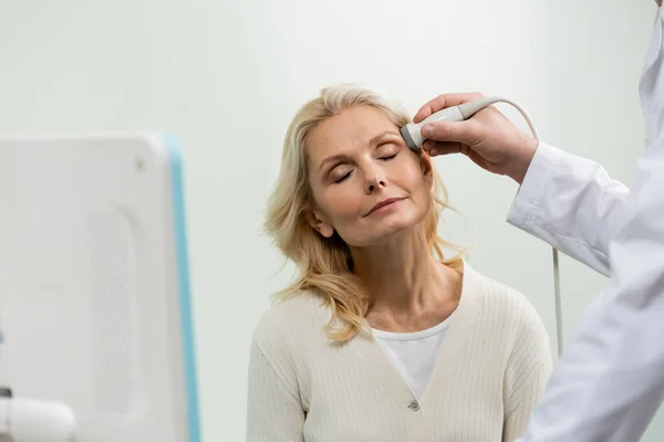 Blondine mit geschlossenen Augen in der Nähe des Arztes beim Kopf-Ultraschall — Stockfoto