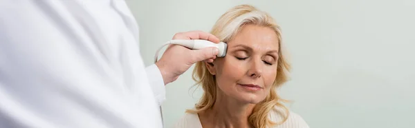 Mujer rubia con los ojos cerrados cerca médico borrosa haciendo ultrasonido de su cabeza, pancarta — Stock Photo
