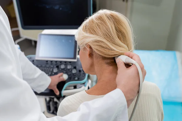 Médico fazendo diagnósticos de mulher loira perto de máquina de ultra-som no fundo borrado — Fotografia de Stock