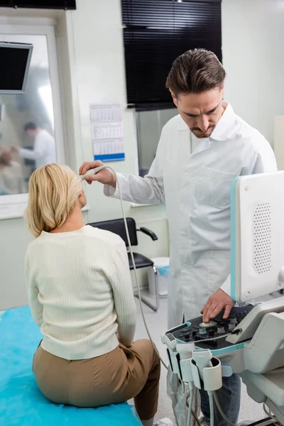 Physician in white coat adjusting ultrasound machine while doing diagnostics of middle aged woman — Stock Photo