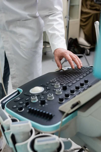 Vista recortada del médico en bata blanca ajustando la máquina de ultrasonido en la clínica - foto de stock
