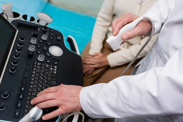 Частковий вид лікаря з використанням консолі ультразвукової машини біля жінки в клініці — стокове фото