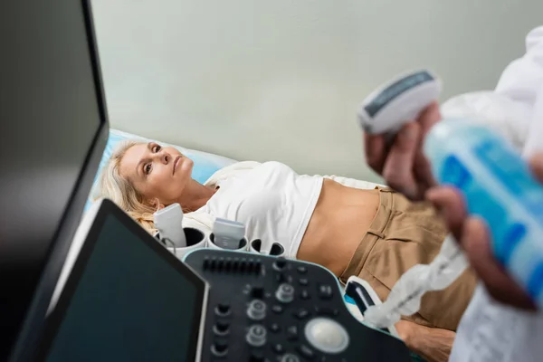 Femme d'âge moyen couché près de la machine à échographie et médecin au premier plan flou — Photo de stock