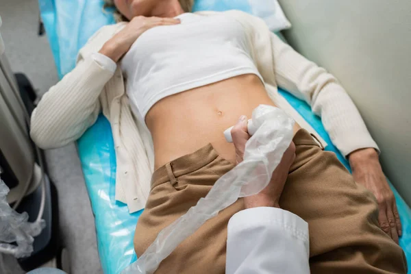 Partial view of woman lying near doctor doing nephrological ultrasound in clinic — Stock Photo