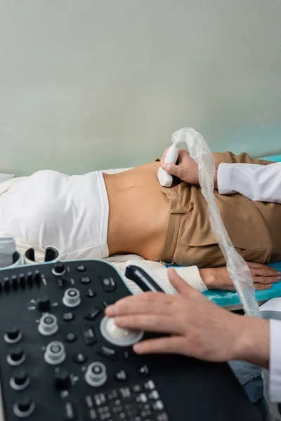 Vista ritagliata del medico che utilizza la macchina ad ultrasuoni durante la diagnostica addominale della donna — Foto stock