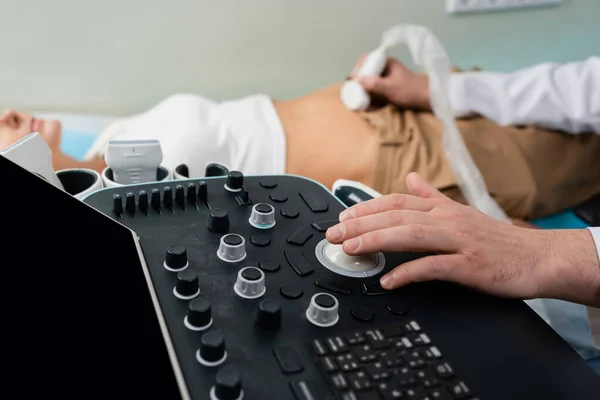 Visão parcial do médico que opera a máquina de ultra-som ao fazer o exame abdominal da mulher desfocada — Fotografia de Stock