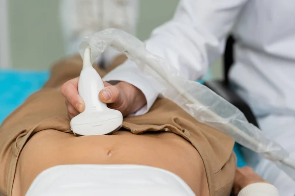 Partial view of blurred doctor holding ultrasound probe near tummy of woman — Stock Photo